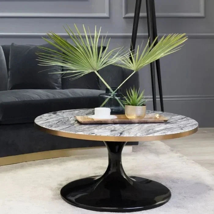 Coffee Table Parme Round. A modern round coffee table with a white and gray marble-patterned top, a gold-toned rim, and a glossy black tulip-style base, styled in a living room setting.